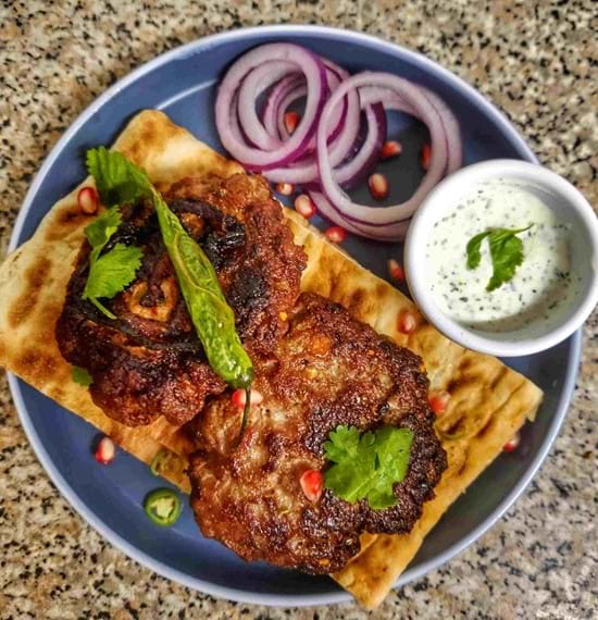 Chapli Kebabs on a blue plate served with red onions