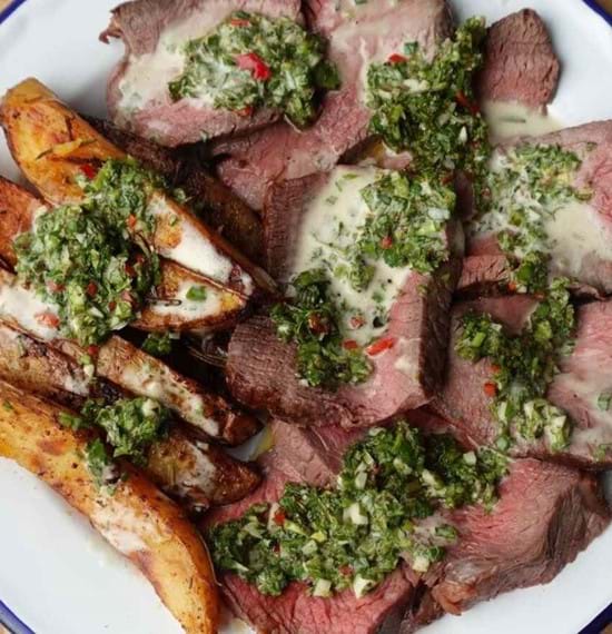 A plate of sliced beef top rump served with chips and chimichurri and bearnaise sauce generously applied