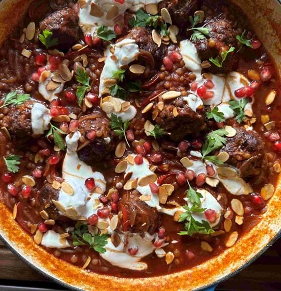 Sticky Pomegranate Beef Meatballs Cooked spiced beef meatballs and giant couscous in a serving dish. Drizzled with yogurt and decorated with pomegranate seeds