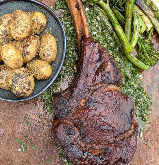 Steak with Lemon and Herb Board Sauce A tomahawk steak on a wooden board served with charred veg