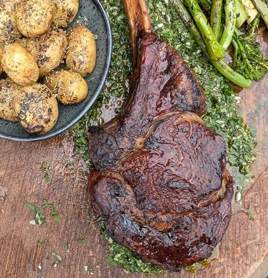 Steak with Lemon and Herb Board Sauce A tomahawk steak on a wooden board served with charred veg